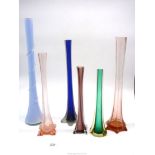 A quantity of coloured single stem vases in blue, pink and green.