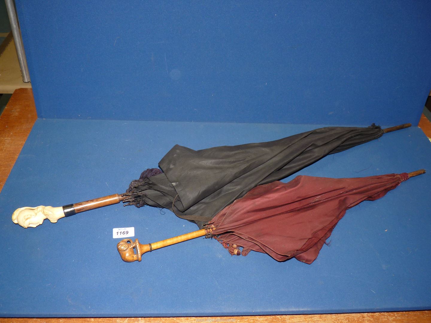 A parasol with wooden shaft and carved elephant handle plus a black umbrella with wooden shaft,