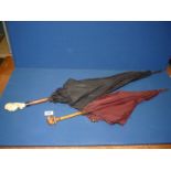 A parasol with wooden shaft and carved elephant handle plus a black umbrella with wooden shaft,