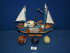 Three polished stone eggs in blue, green and brown and a small model of a fishing boat.