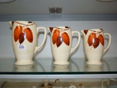 Three graduated 'Autumn leaves' jugs, (small chips to rims), by Clarice Cliff for J. Wilkinson Art.