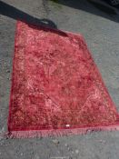 A bordered, patterned and fringed rug, red ground, green stylized floral motif (some paint marks),
