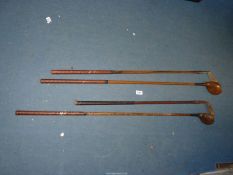 Three Hickory golf clubs including two woods and an iron, plus another iron.