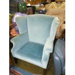 A pale blue upholstered wing Fireside Armchair standing on moulded square front legs (small tear to