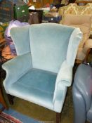 A pale blue upholstered wing Fireside Armchair standing on moulded square front legs (small tear to