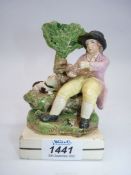 A Staffordshire pottery figure of a man sitting by a tree with his dog by his side waiting for food