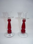 A pair of ruby red candlesticks with rounded undulating stems and clear rims and bases,
