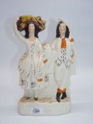 A Staffordshire flatback of a couple with the lady carrying bales of fabric on her head, 12" tall.