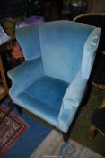 A pale blue upholstered wing Fireside Armchair standing on moulded square front legs (small tear to