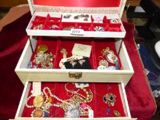 A cream jewellery box and contents including; costume brooches, earrings, bracelets, etc.
