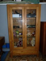 A contemporary light Oak display cabinet having a pair of opposing glazed doors,