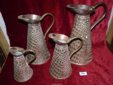 A graduated set of four copper jugs, with crocodile skin effect.
