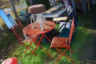 A circular metal table and two chairs, and a three legged cast iron stool.