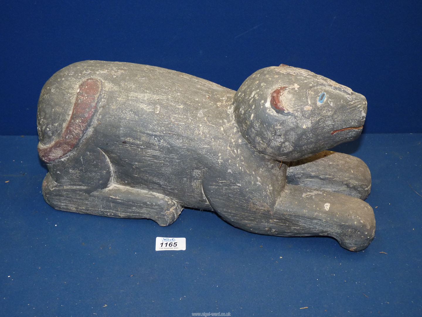 A heavy carved wooden figure of a stylized feline with painted details to the eyes, ears and tail,