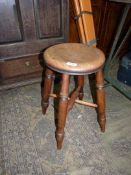 A rustic circular Elm seated stool raised on four turned Ash wood legs with a cross stretcher,