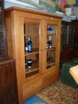 A contemporary light oak display cabinet/bookshelves having a pair of opposing glazed doors over a