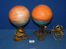 A pair of contemporary lamps with orange globe shades standing on metal three dolphin stand,