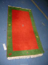 An Indian carpet, red ground with green border, 6' x 3'.