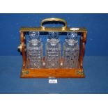 A Betjemann's wood and brass Tantalas with three cut glass decanters, makers Lloyd Payne Amie,