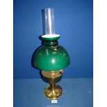 A brass based oil lamp having glass chimney and green domed shade.