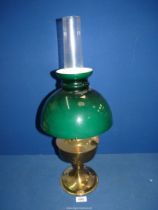 A brass based oil lamp having glass chimney and green domed shade.