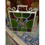 An early 20th century scroll frame, brass fireguard enclosing a stained glass panel, 38" x 18".