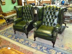 A pair of elegant green Leather upholstered Wing Fireside Chairs having buttoned backs and shaped