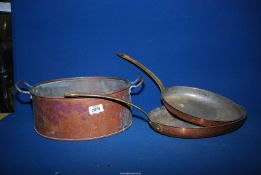 A copper pan plus two oval copper frying pans having brass handles.