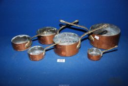 A set of six graduated copper pans having brass handles.