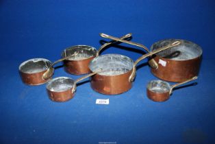 A set of six graduated copper pans having brass handles.