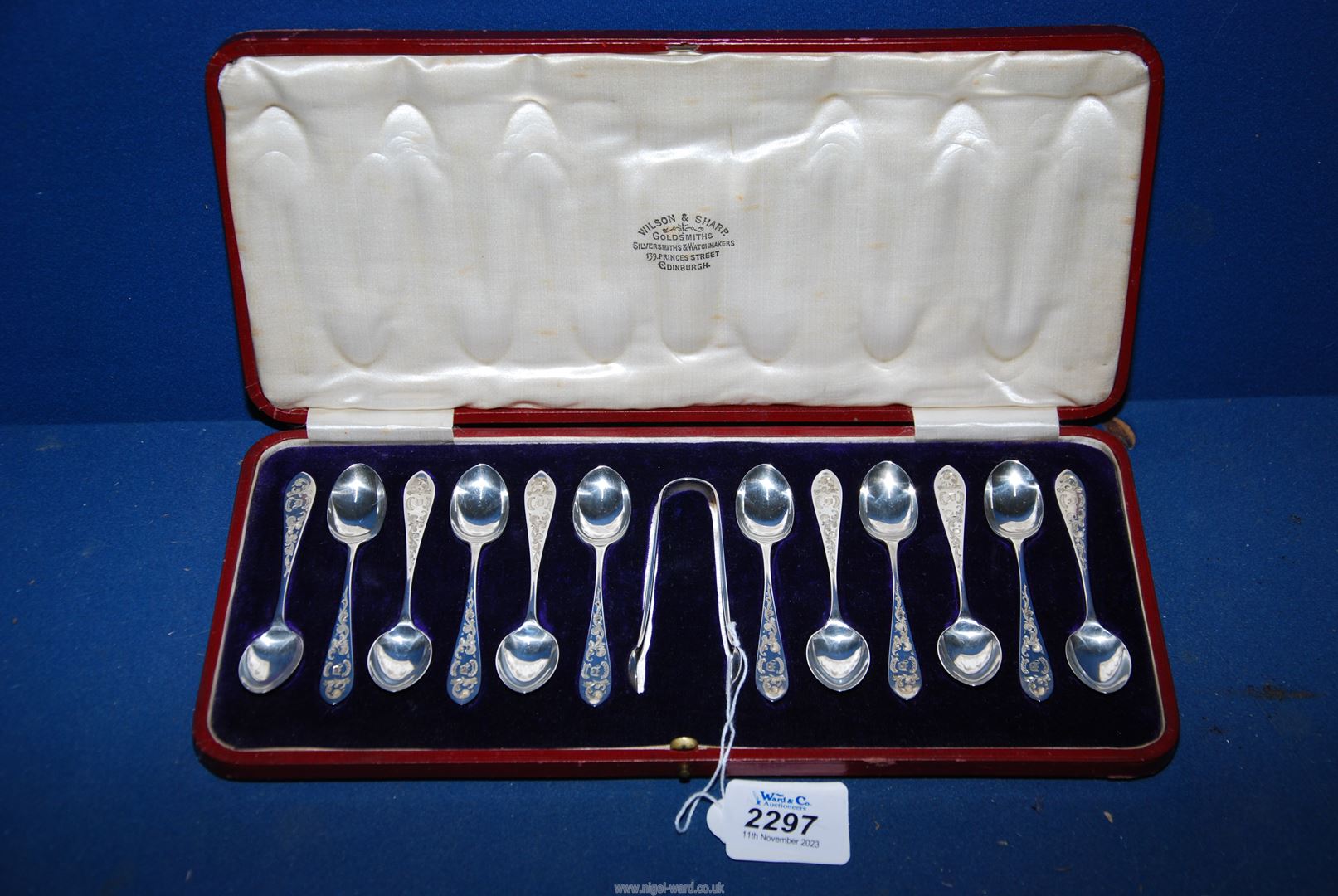 A set of twelve Silver coffee spoons and sugar tongs having engraved scroll decoration and in a red