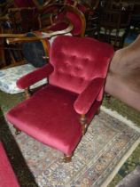 A maroon buttoned upholstered open armed easy Chair standing on turned front legs and having brass