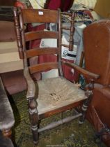 An antique high ladder back open armed Armchair having a distressed rush seat,