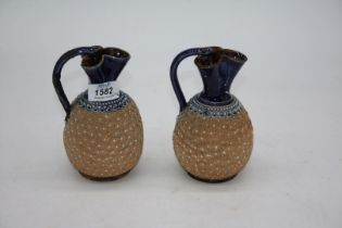 A pair of Doulton Lambeth ewer style jugs having trefoil shaped tops, one handle repaired, 6" tall.