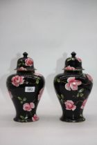 A pair of Thomas Till & Sons lidded vases having black ground with pink rose blooms and trailing