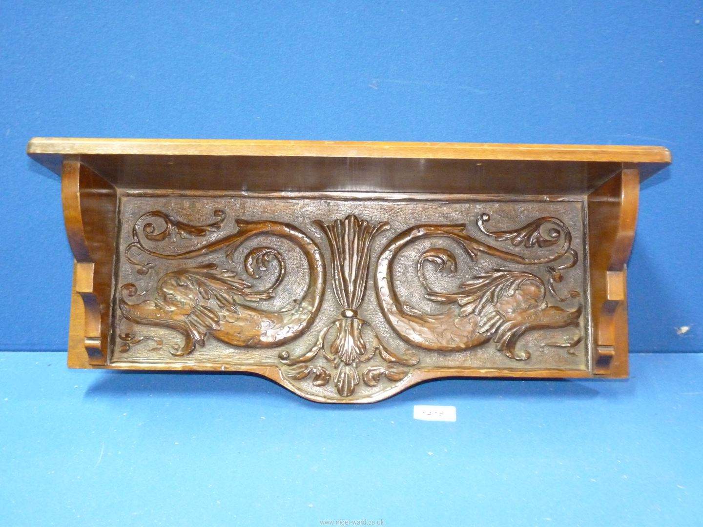 A carved wood wall shelf with stylised fish and foliage decoration,