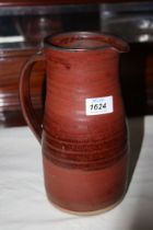 A russet red Studio Pottery jug with purple brush abstract marks to front,