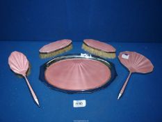 A vintage dressing table set in pink enamel comprising tray, two clothes brushes,