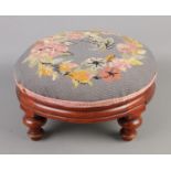 A needlepoint embroidered foot stool depicting floral spiral raised on rosewood base with turned