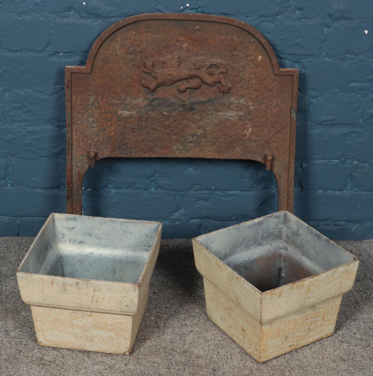 A cast iron fireplace back with lion decoration along with a pair of cast iron drain hoppers.