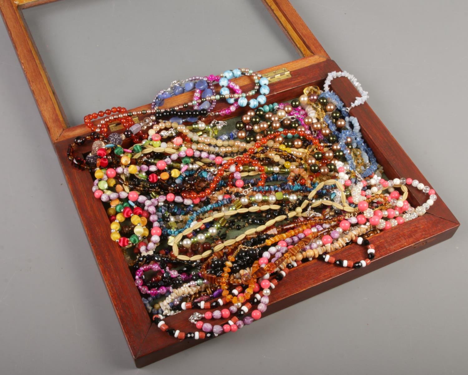 A bijouterie cabinet with contents of a large quantity of necklaces and bracelets. Includes glass