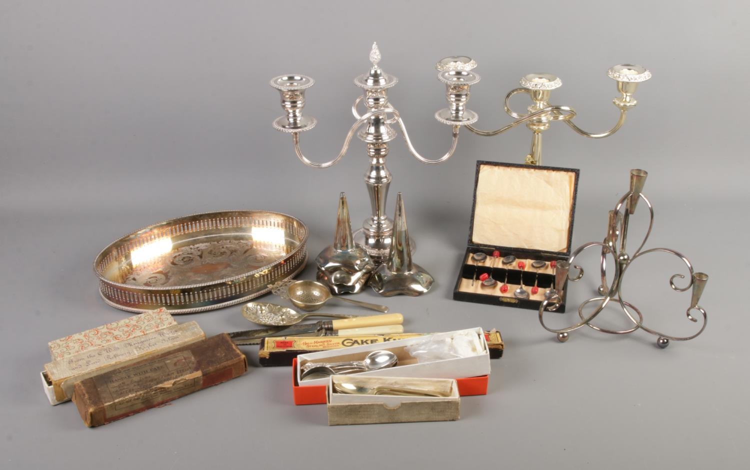 A box of assorted silver plate including candlestick, cake knives and commemorative spoons.