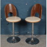 A pair of swivel bar chairs with wooden backs and chrome supports.