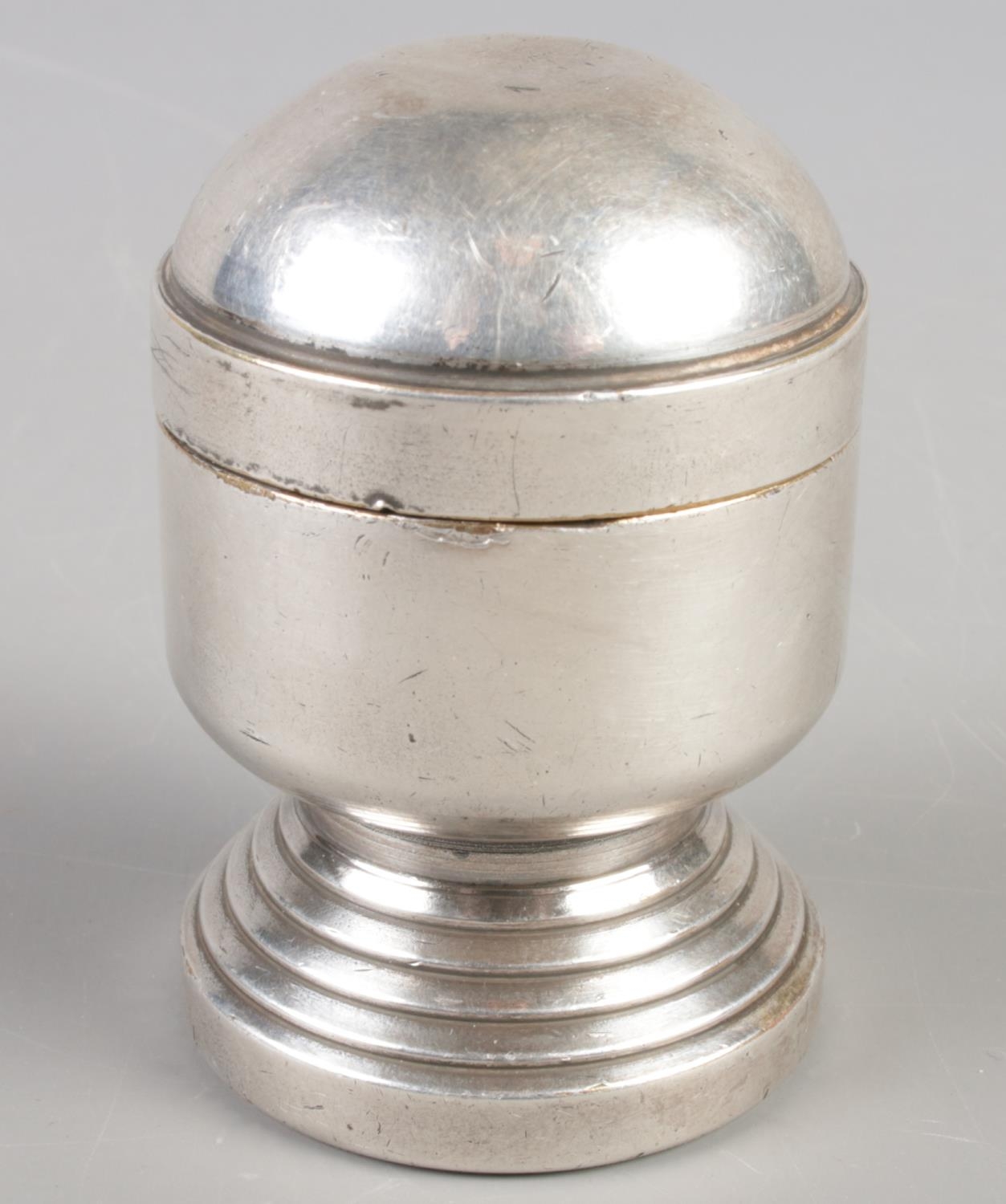 A white metal table lighter raised on circular stepped base. (8cm)
