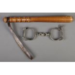 A turned wood truncheon (40cm) along with a pair of antique police handcuffs with key.