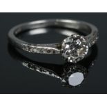 A platinum and diamond ring. The larger stone flanked by diamond set shoulders. Size L 1/2. 2.91g.