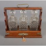 A three decanter tantalus with key featuring silver plated labels with Lion head decoration.
