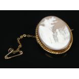 A 9ct Gold cameo brooch, with safety chain, depicting a woman in a village setting. Total weight: