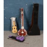 A collection of musical instruments including Mahalo purple Ukelele, Sitar and one other Ukelele.