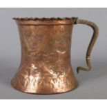 A large hammered copper tankard with wavy edge and beaten decoration depicting deer and flowers.